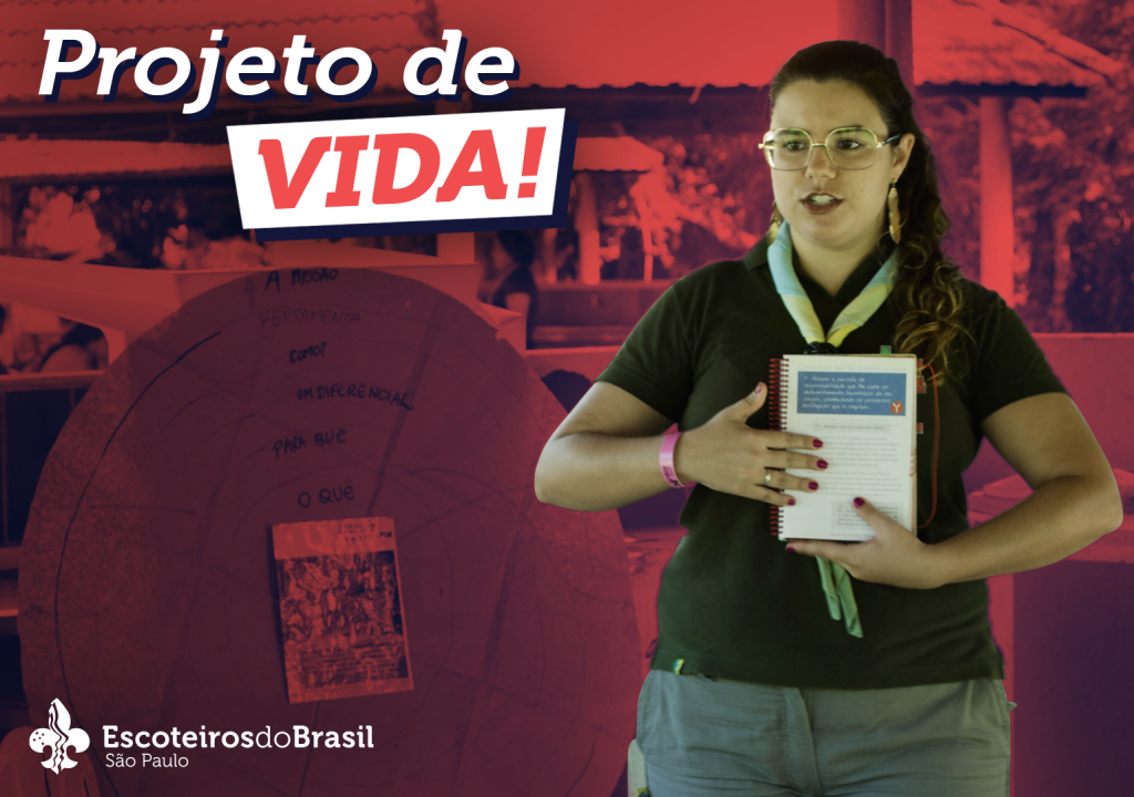 Foto com texto no canto superior esquerdo "Projeto de Vida!", no canto inferior esquerdo o logo da Escoteiros do Brasil São Paulo. Do lado direito uma mulher branca aparece da cabeça até a altura da coxa. O cabelo loiro escuro e ondulado está amarrado em rabo de cavalo jogado sobre o ombro esquerdo. Usa óculos retangulares com armação prata, lenço escoteiro da nacional e camisa polo verde. Com as mãos na altura da barriga, segura um livro.