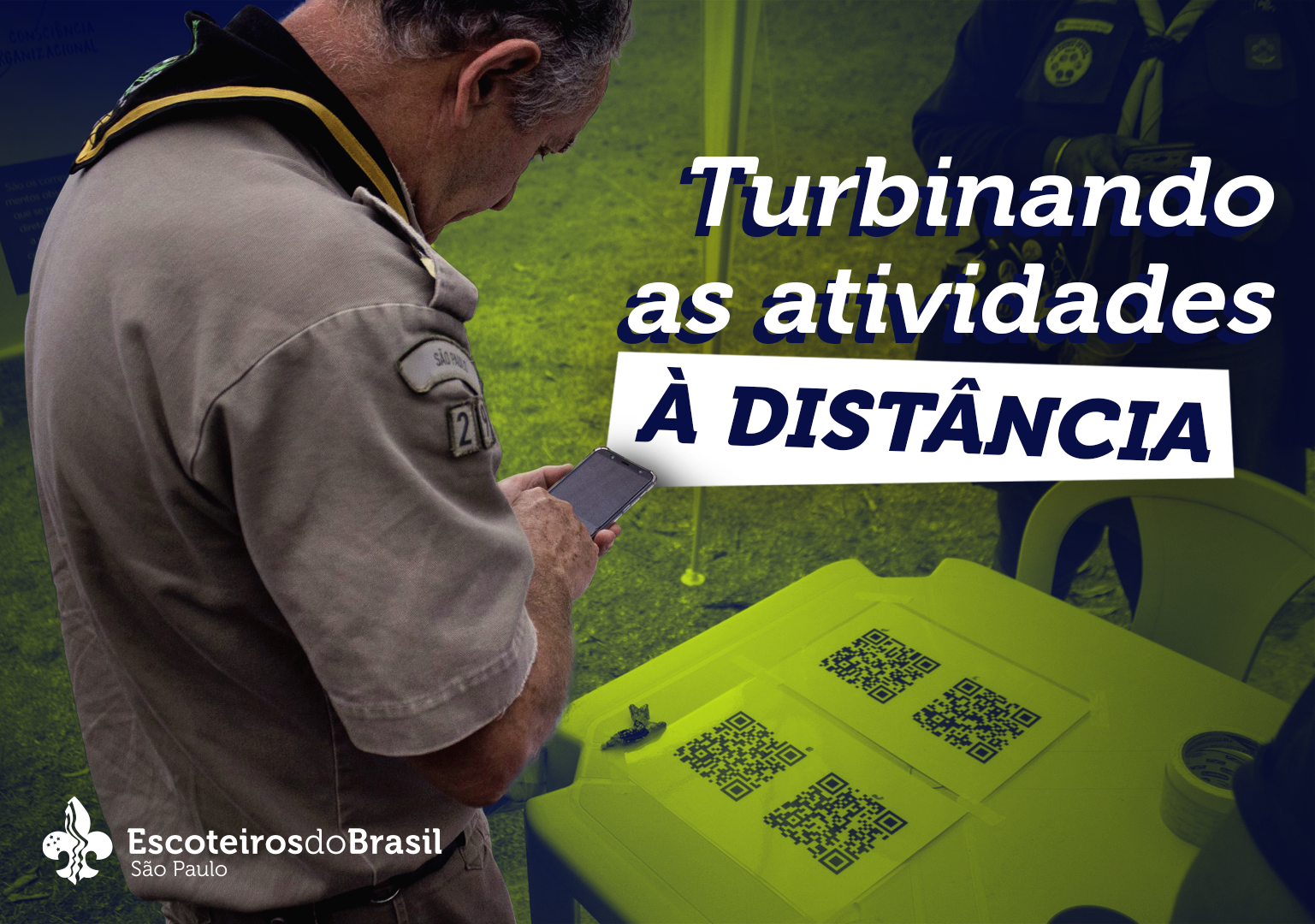 Foto com um homem em pé do lado esquerdo posicionado de lado da cabeça até a cintura. Está com a cabeça abaixada, tem cabelos curtos e grisalhos. Usa lenço escoteiro preto com detalhe amarelo e uniforme cáqui. Segura um celular com a mãos esquerda e está com a mãos direita sobre ele. Em sua frente há uma mesa e sobre ela duas folhas com dois QR Code cada. No canto superior direito o texto em branco: Turbinando as atividades à distância. No canto inferior esquerdo o logo da Escoteiros do Brasil São Paulo.