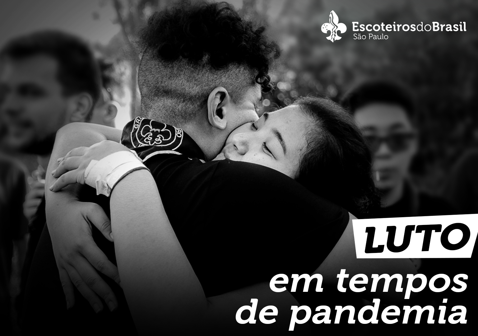 Foto em preto e branco de dois jovens escoteiros se abraçando. No canto superior direito o logo da Escoteiros do Brasil São Paulo e no canto inferior direito escrito "Luto em temos de pandemia".